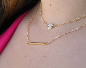 May include: A gold layered necklace with a thin bar pendant and a small round pendant.