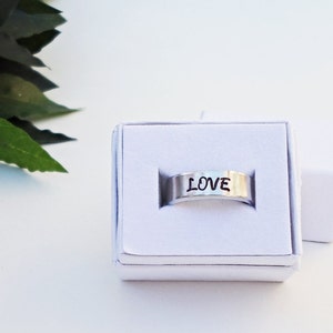 May include: A silver ring with the word "LOVE" engraved on it. The ring is in a white box.