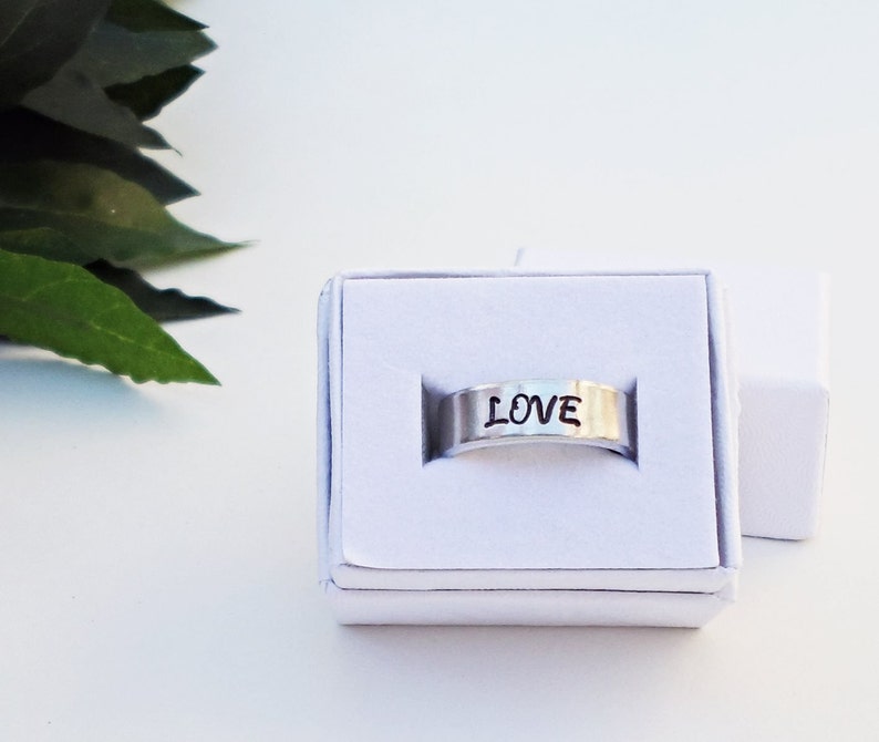 May include: A silver ring with the word "LOVE" engraved on it. The ring is in a white box.