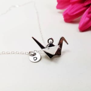 May include: Silver necklace with a silver origami crane pendant and a silver charm with the letter 'D' on it.