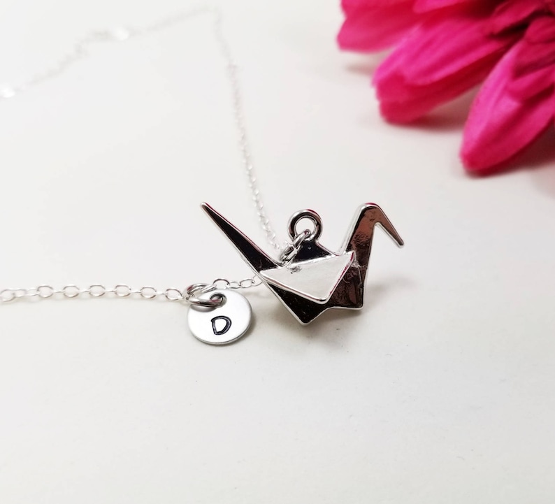 May include: Silver necklace with a silver origami crane pendant and a silver charm with the letter 'D' on it.