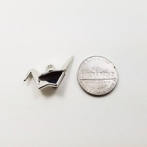 May include: A silver origami crane charm, next to a US five-cent coin.