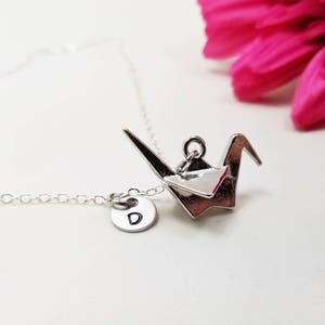 May include: Silver necklace with a silver origami crane charm and a silver disc charm with the letter 'D' engraved on it.
