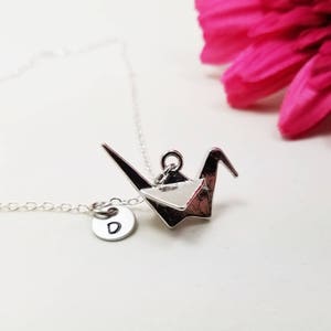 May include: A silver necklace with a silver origami crane pendant and a small silver charm with the letter 'D' on it.