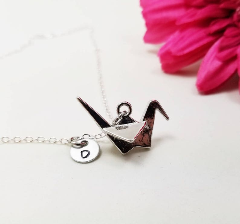 May include: A silver necklace with a silver origami crane pendant and a small silver charm with the letter 'D' on it.