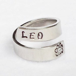 Könnte beinhalten: Silberring mit der Gravur "LEO" auf dem Band. Der Ring ist im Wickelstil mit einem Löwenkopfdesign an der Seite.