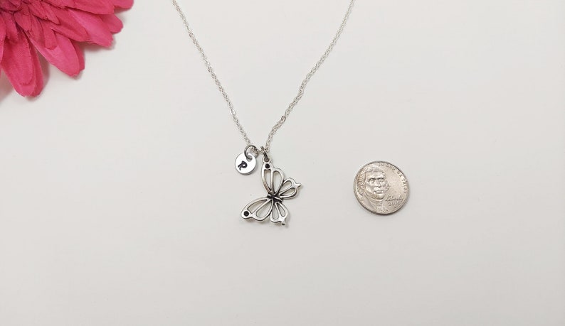 K&ouml;nnte beinhalten: Eine silberne Schmetterlingskette mit einem kleinen silbernen Diskus-Anh&auml;nger. Der Diskus-Anh&auml;nger tr&auml;gt den eingravierten Buchstaben 'P'. Die Kette wird neben einer US-Dollar-M&uuml;nze zur Gr&ouml;&szlig;envergleich gezeigt.