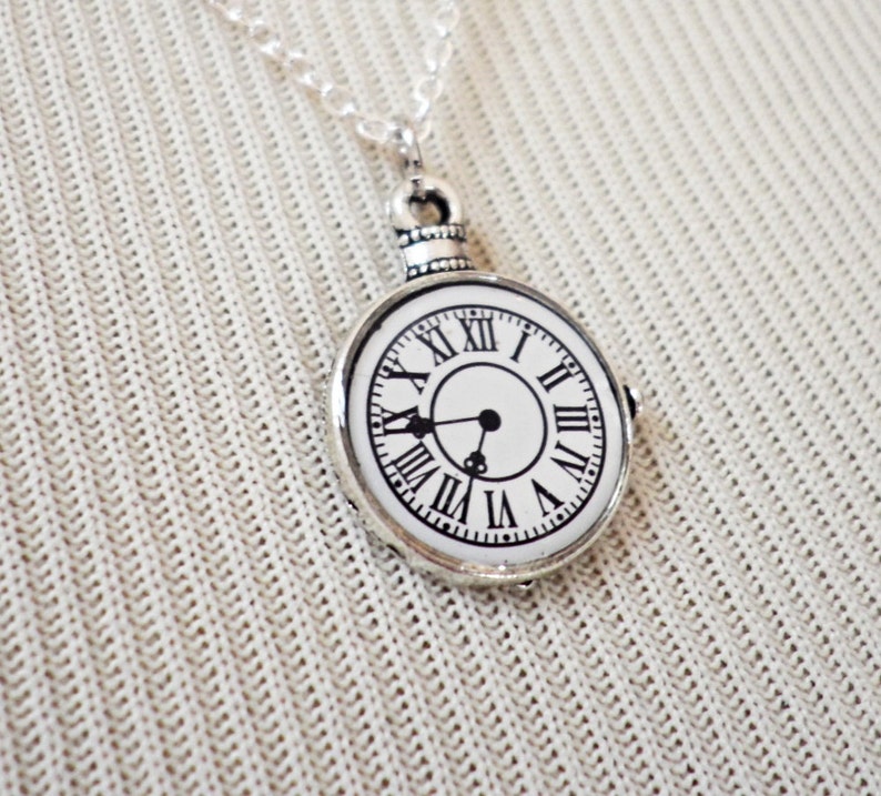 May include: A silver necklace with a round clock pendant. The clock face is white with black Roman numeral markings and black hands.