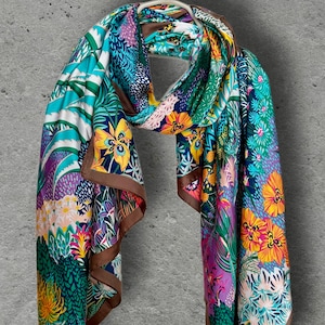 Peut inclure: Un foulard rectangulaire orné d'un imprimé botanique vibrant composé de fleurs jaunes, orange et roses sur un fond de feuillage bleu sarcelle, vert et violet. Le foulard est doté d'une bordure marron unie sur les bords du tissu.