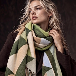 May include: A long, rectangular scarf featuring a geometric pattern of large triangles in shades of forest green, olive, beige, and pale blue. The scarf has a textured knit appearance and includes a fringe detail along the bottom edge.