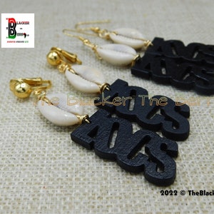 May include: Black wooden earrings with the word "40s" cut out, paired with white seashells and gold-colored hardware. The earrings are displayed on a textured, tan surface. The Blacker The Berry logo is in the upper left corner.