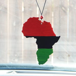 May include: A red, black, and green car air freshener shaped like the continent of Africa. The air freshener is hanging from a rearview mirror.