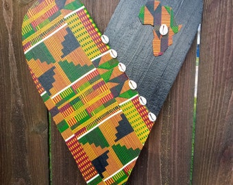 May include: A wooden heart-shaped sign with a black and white African continent design on one side and a colorful African print on the other side. The sign is decorated with white seashells.