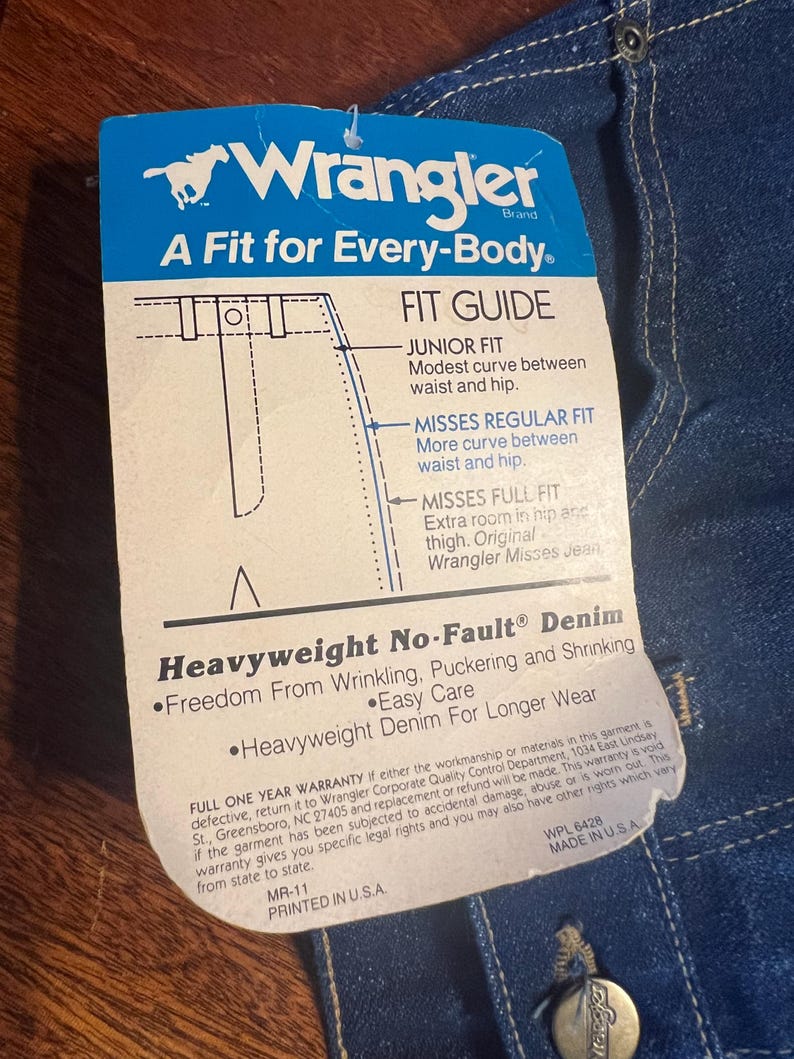 May include: A blue and white Wrangler brand tag with the text "A Fit for Every-Body" and a fit guide. The tag also states "Heavyweight No-Fault Denim" and "Freedom From Wrinkling, Puckering and Shrinking."