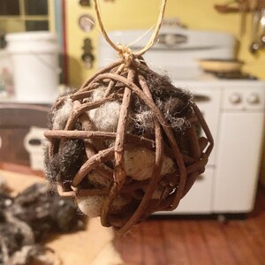 May include: A handcrafted sphere ornament made of woven brown twigs, enclosing a mix of white and dark gray wool. A natural twine loop is attached for hanging. The rustic design suggests a focus on natural materials and home decor.