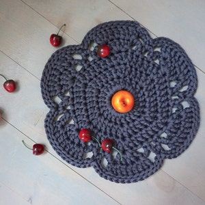 以下が含まれることがあります： 円形のデザインと複雑なディテールを持つダークグレーのクロシェレース。レースは赤いチェリーとオレンジ色のリンゴ1つで飾られています。