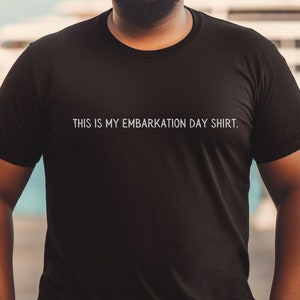 May include: A man wearing a black t-shirt with the text "THIS IS MY EMBARKATION DAY SHIRT."  He is standing on a wooden dock with a large white yacht in the background.