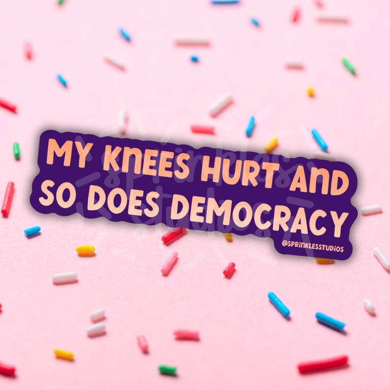 May include: A purple sticker with the text "MY KNEES HURT AND SO DOES DEMOCRACY" in white and orange. The sticker is surrounded by colorful sprinkles on a pink background. The sticker also includes the text "@SPRINKLESSTUDIOS".