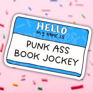 May include: A blue name tag sticker with the text "Hello, my name is Punk Ass Book Jockey".
