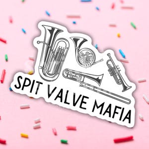 May include: A black and white sticker with a graphic of four brass instruments, including a tuba, a french horn, a trombone, and a trumpet. The text "SPIT VALVE MAFIA" is written below the instruments.