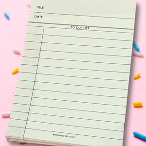 May include: A white lined notepad with the words "TO DUE LIST" written on it. The notepad has spaces for a title and date. The notepad is on a pink background with colorful sprinkles.