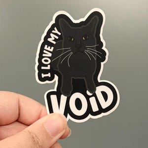 May include: A die-cut sticker featuring a black cat with yellow-green eyes and white whiskers. The text "I LOVE MY" is arched above the cat, and the word "VOID" is printed in large white letters at the bottom, all outlined in black and white.