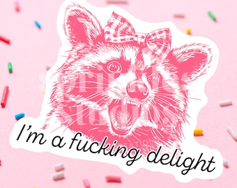 May include: A pink sticker featuring a detailed illustration of a raccoon with an open mouth and a checkered bow. The sticker has the text "I'm a fucking delight" in a cursive font. The background is pink with colorful sprinkles.