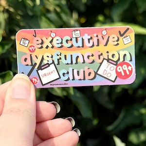 Könnte beinhalten: Ein rechteckiger Aufkleber mit regenbogenfarbenem Hintergrund und dem Text "executive dysfunction club" in einer abgerundeten Schriftart. Das Design enthält Illustrationen von Aufgabenlisten, Uhren und roten Kreisen mit der Aufschrift "99+".