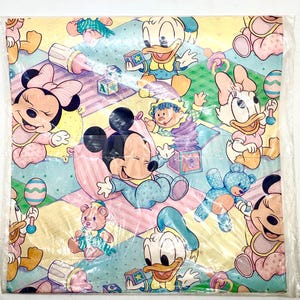 May include: A square sheet of baby-themed wrapping paper featuring cartoon characters Mickey Mouse, Minnie Mouse, Donald Duck, and Daisy Duck. The characters are in pastel colours, surrounded by toys and blocks on a checkered background.