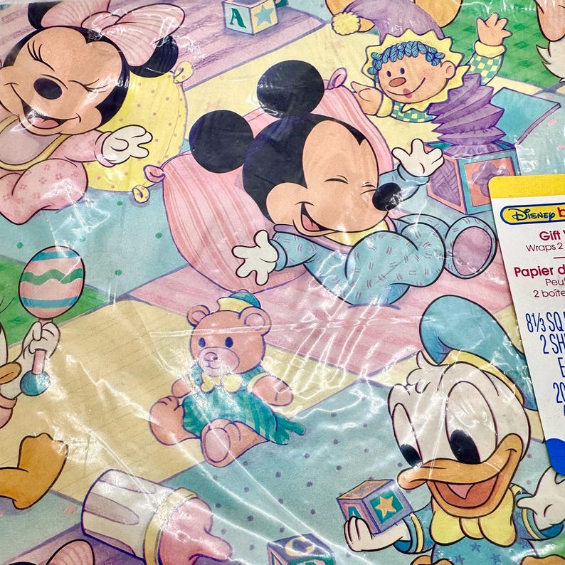 May include: Disney baby gift wrap featuring Mickey Mouse, Minnie Mouse, Donald Duck, and a teddy bear. The wrapping paper has a pastel colour scheme with a repeating pattern of the characters and baby-related items. The packaging includes the text "Disney Baby Gift Wraps".
