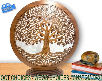 May include: A circular wooden wall art piece featuring a laser-cut tree of life design with intricate branches, leaves, and roots. The piece stands on a tiered circular base. Below the art, the text reads: ROOT CHOICES - WOOD CHOICES - CUSTOM TEXT.