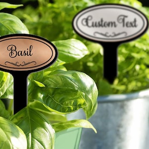 May include: Two black metal plant markers with oval-shaped copper and silver labels. The copper label says "Basil" and the silver label says "Custom Text".