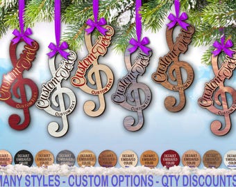 Pode incluir: Seis ornamentos de madeira em forma de clave de sol com vários acabamentos de grão de madeira, cada um com um laço de fita roxa no topo e o texto Custom Text gravado. Uma fila de amostras de cores circulares é exibida na parte inferior.