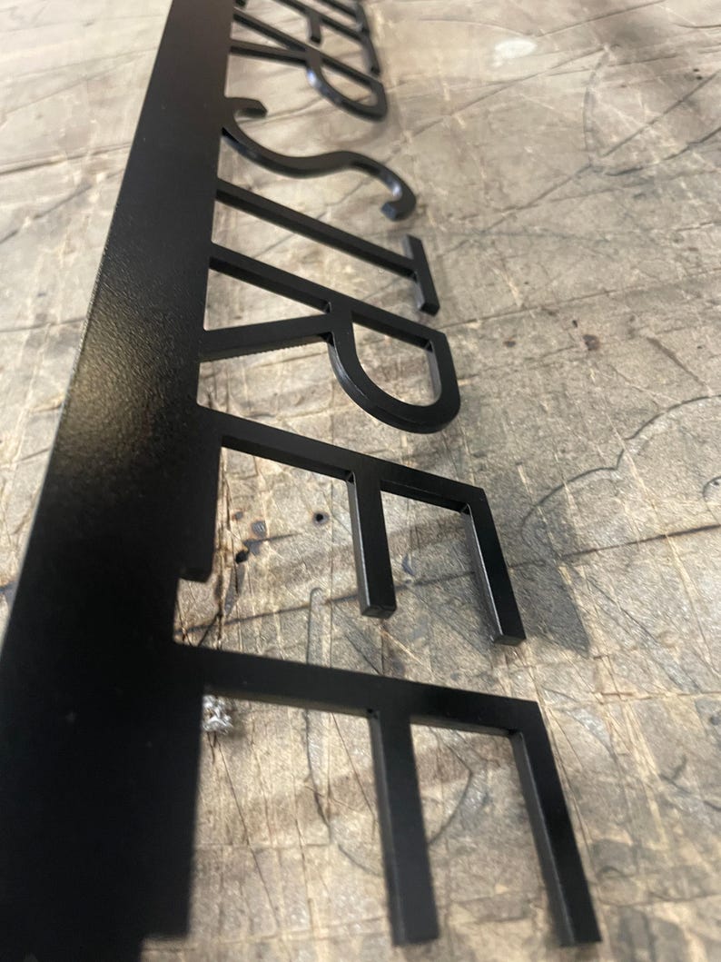 A close-up, side-angle view of the black metal sign, showing the laser-cut letters "STREET" with a slight shadow beneath them on a gray surface.
