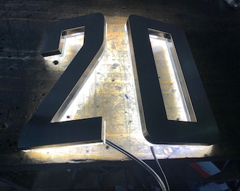 May include: Two illuminated metal numbers, 20, with a white light shining through the cut-out letters. The numbers are on a wooden surface.