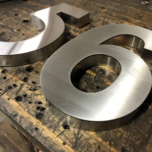 Two brushed metal numbers, a "5" and a "6", rest on a dark, scratched wooden surface.