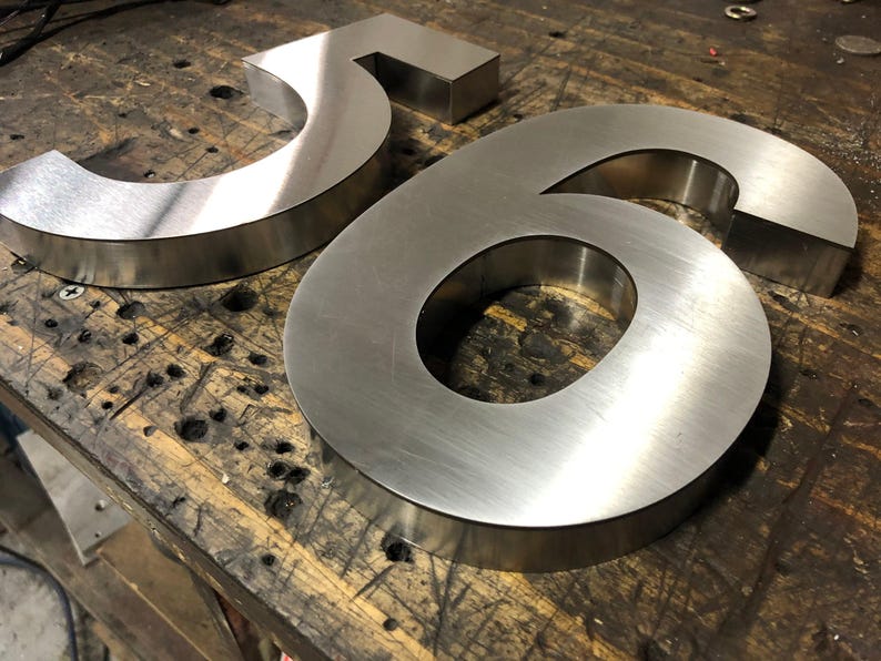 Two brushed metal numbers, a "5" and a "6", rest on a dark, scratched wooden surface.