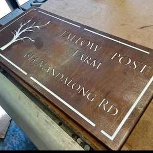 Puede incluir: Un letrero de metal oxidado con un borde blanco y letras blancas. El letrero dice "Tallow Post Farm" y "614 Mandalong Rd". Un árbol estilizado está en la esquina superior izquierda.