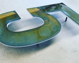 May include: A close-up of the number 51 made of metal with a green and brown patina. The numbers are mounted on a white surface.
