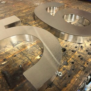 Two brushed metal numbers, a "5" and a "6", rest on a dark, scratched wooden surface, viewed from an angle.