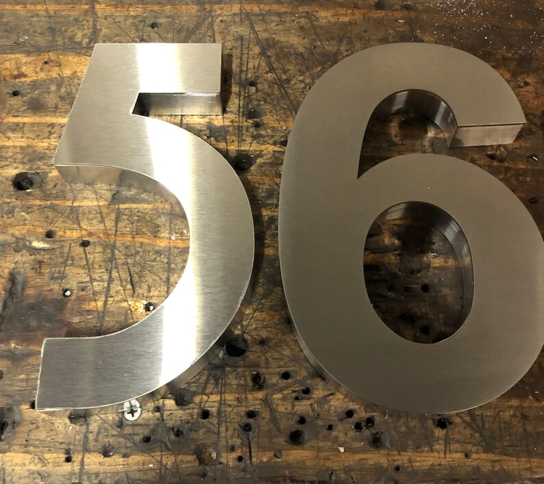 Two brushed metal numbers, a "5" and a "6", are placed side-by-side on a dark, scratched wooden surface.