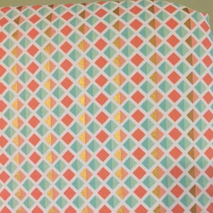 May include: A white fabric with a repeating pattern of coral and mint green diamonds with gold accents.