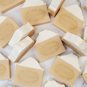May include: A collection of beige and white handmade soap bars with the text "Dermalicious" printed on each bar.