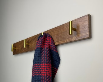 May include: A wooden wall-mounted coat rack with four gold hooks. A red and black plaid scarf is hanging on one of the hooks.