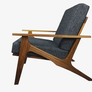 May include: A mid-century modern armchair with a dark gray fabric upholstery and a wooden frame. The chair has a unique angled design with a wide, comfortable seat and back.
