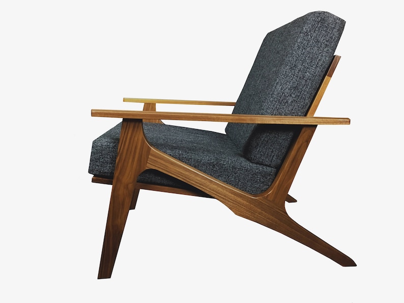 May include: A mid-century modern armchair with a dark gray fabric upholstery and a wooden frame. The chair has a unique angled design with a wide, comfortable seat and back.