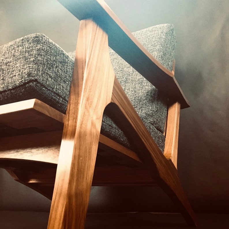 May include: A wooden armchair with a gray fabric seat and back. The chair has a unique, angled design with a wide, flat armrest.