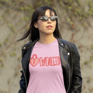 May include: A pink t-shirt with a red heart and the word "OWNED" in red letters. The heart has a keyhole in it.