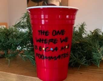 May include: Red plastic cup with the text "The One Where We Became Roommates" in black lettering. The text "became" has colorful dots in the letters.