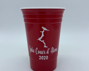 May include: Red plastic cup with a white outline of Lake Coeur d'Alene and the text "Lake Coeur d'Alene 2020".